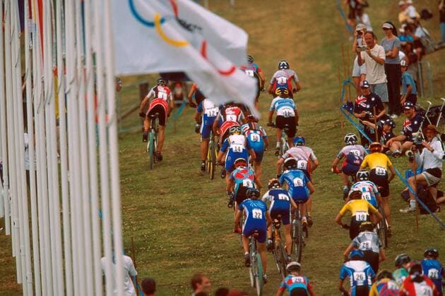 Mountainbikerinnen fahren unter der olympischen Flagge einen Anstieg hinauf Mountainbike OS Sommer Damen Olympische Sommerspiele 2000, Spiele, Olympia, Olympiade, MTB, Mountainbiking, Cross Country Totale Mountain Bike Course Fairfield, Crosscountry Sydney