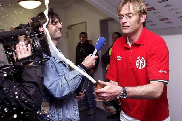 Trainer Jürgen Klopp (Mainz) nimmt beim Korkenknallen keine Rücksicht auf die Kamera der ARD, der Reporter nimmt es gelassen Fußball 2. BL Herren Saison 2003 2004, FSV Mainz 05, Aufstieg, Aufsteiger, Aufstiegsfeier, Feier, Kabinenfeier, Kabine, Gruppe Mainz Freude, Begeisterung,