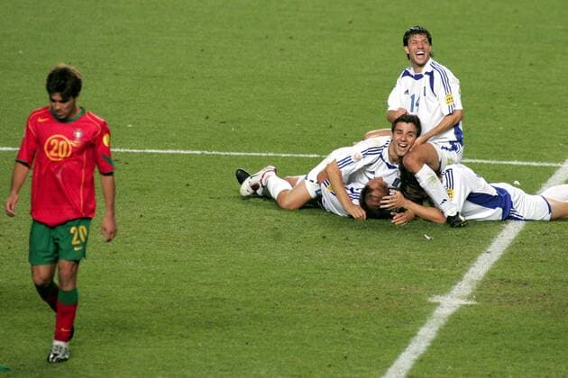 Fußball, EM Finale 2004 in Lissabon, Portugal - Griechenland 0:1 Die Sieger feiern, der Verlierer schleicht von dannen - Panagiotis Fyssas (sitzend), Konstantinos Katsouranis (li.), Basinas (li.unten) und Seitaridis (alle Griechenland wälzen sich überglücklich am Boden, Deco (Portugal) zieht ab Fußball EM Herren Euro 2004, Europameisterschaft, Länderspiel, Nationalmannschaft, Nationalteam, Finale, Trikot, Gruppe pan6530 Lissabon Glück, Begeisterung, Freude,  
