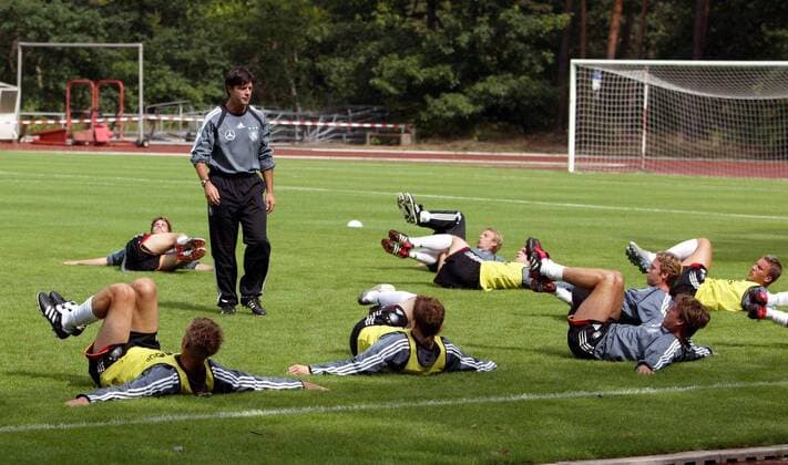 Co-Trainer Joachim Löw (Mitte) überwacht die Dehnungsübungen der Spieler, Bundestrainer Jürgen Klinsmann (beide Deutschland, hinten) macht die Übungen am Boden liegend mit Fußball Herren Nationalmannschaft 2004, Nationalteam, Training, Vorbereitung Gruppe Frankfurt M.