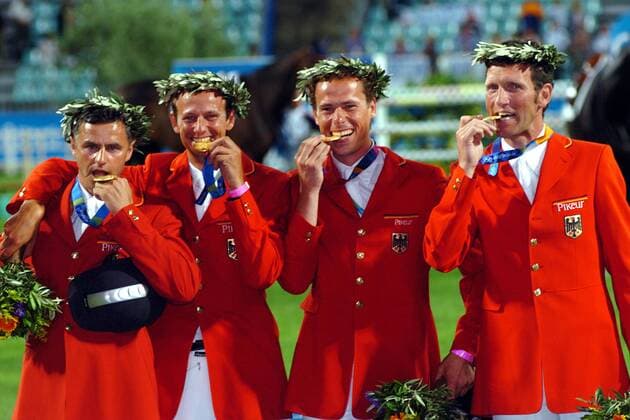 Die deutsche Equipe ist Olympiasieger, v. re.: Ludger Beerbaum, Christian Ahlmann, Marco Kutscher und Otto Becker (alle Deutschland) beißen in ihre Goldmedaillen Pferdesport OS Sommer Herren Olympische Sommerspiele Athen 2004, Olympia, Olympiade, Spiele, Reiten, Reitsport, Springreiten Gruppe Markopoulo Freude,