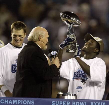Wide Receiver Deion Branch (New England Patriots) präsentiert die Vince Lombardi Trophäe während er mit Fox Reporter Terry Bradshaw spricht; li. Quarterback Tom Brady - (Icon5923113) American Football Herren NFL 2004 2005, SuperBowl, Super Bowl, Endspiel, Finale Gruppe Jacksonville Begeisterung, Freude, EDITORIAL USE ONLY