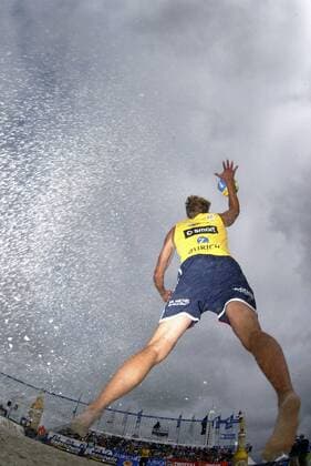 Ein Beachvolleyballer schlägt unter wolkenverhangenem Himmel eine Aufgabe Beachvolleyball Herren Zürich Masters 2005, Zurich, Zuerich, Beach Einzelbild Sprungangabe, Sprungaufschlag, Angabe St. Peter Ording Dynamik,