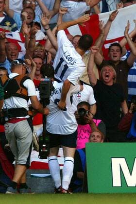 Wayne Rooney (unten) trägt Torschütze Joe Cole (beide England) jubelnd auf den Schultern vor den englischen Fanblock -  Fußball Länderspiel Herren Weltmeisterschaftsqualifikation 2005, Nationalmannschaft, Nationalteam, Länderspiel, Qualifikation Totale Nationaltrikot Cardiff Freude, Begeisterung,