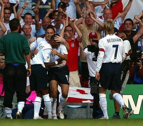 Torjubel vor dem englischen Fanblock - Ashley Cole (li.) und Torschütze Joe Cole (Mitte) umarmen sich, daneben kommt David Beckham (alle England) hinzu -  Fußball Länderspiel Herren Weltmeisterschaftsqualifikation 2005, Nationalmannschaft, Nationalteam, Länderspiel, Qualifikation Totale Nationaltrikot Cardiff Harmonie, Freude, Begeisterung,