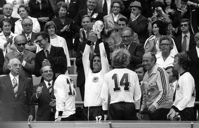 Weltmeister BR Deutschland - Wolfgang Overath (Mitte) jubelt mit dem WM Pokal, daneben u.a. vorn: DFB Präsident Hermann Gösmann (li.), Gerd Müller (3.v.li.), Uli Hoeneß (3.v.re.), Bundestrainer Helmut Schön (2.v.re.) und Bernd Hölzenbein (re.) Fußball WM Herren Weltmeisterschaft 1974, Nationalmannschaft, Nationalteam, Nationaltrikot, Länderspiel, Finale Totale Ehrentribüne, Tribüne, Tribünen München, Zuschauer, Publikum Glück, Begeisterung, Freude,