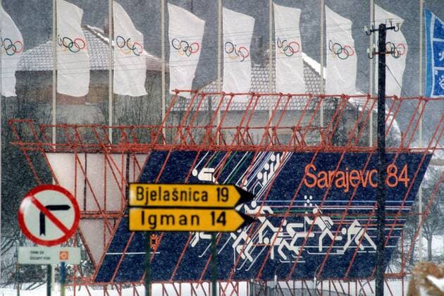 Das winterliche Sarajevo präsentiert sich ganz im Zeichen Olympias: die Verkehrsschilder zeigen die Entfernung zu den Wettkampfstätten am Bjelasnica und am Igman, dahinter sind die Sportarten in Piktogrammen dargestellt OS Winter Damen Olympische Spiele 1984, Winterspiele, Vdia Totale Sarajevo