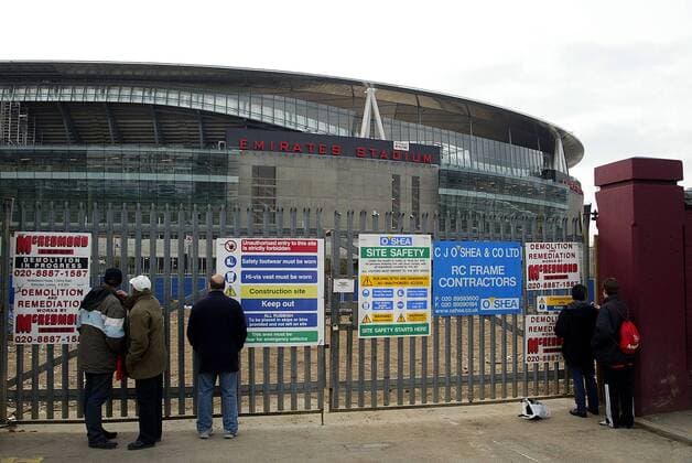 Fußballfans betrachten durch einen mit Sicherheitshinweisen bestückten Zaun das sich noch im Bau befindliche Emirates Stadium, zukünftige Spielstätte von Arsenal London -  Fußball Herren English Premier League 2005 2006, 1. Englische Liga, Arsenal FC London, Stadionneubau, Neubau Totale Emirates Stadium London