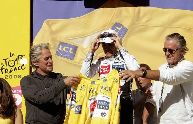 Carlos Sastre (Spanien CSC) schlüpft nach seinem Etappensieg bei der 17. Etappe der Tour de France 2008 von Embrun nach L Alpe d Huez ins gelbe Trikot, die Ehrung vollziehen Schauspieler Michael Douglas (li.) und Basketballtrainer Pat Riley (beide USA) Radsport Herren Tour de France 2008, Straßenradsport, Straße, Rad, Gruppe 17. Etappe: Embrun - L Alpe d Huez, lAlpe dHuez