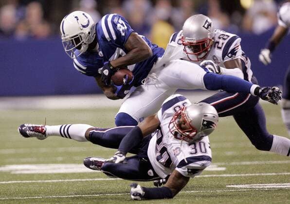 Indianapolis Colts wide receiver Reggie Wayne (87) is tripped up by New England Patriots defenders Brandon McGowan (30) and Darius Butler (28) during the second quarter at Lucas Oil Field in Indianapolis on November 15, 2009  IND2009111507