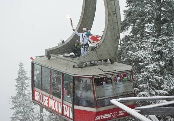 Canadian Olympic Snowboard Team member Justin Lamoureax holds the torch as he rides up on the roof of the Grouse Mountain Skyride on Day 104 of the Vancouver 2010 Winter Olympic Torch Relay above North Vancouver, British Columbia, February 10, 2010. -  OLY20100210713 o0 Gondel, Dach, Gondeldach, Fackel, Feuer,