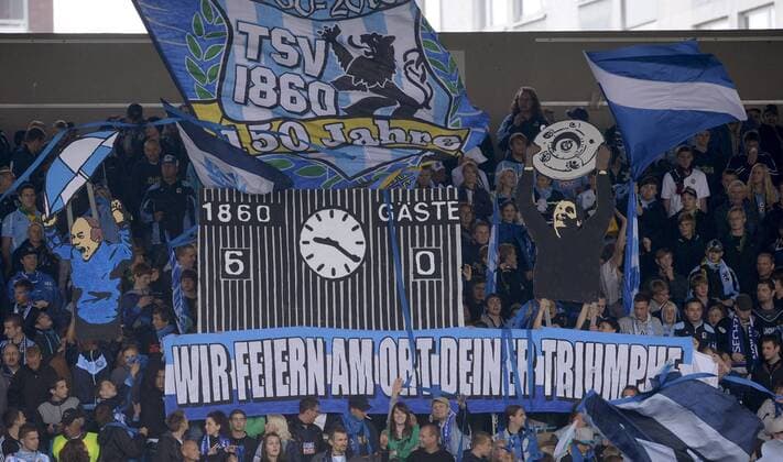 24.07.2010, Testspiel im Grünwalder Stadion, TSV 1860 München, Wir feiern am Ort deiner Triumphe - das Transparent halten die Fans in die Höhe und Ein Bild von Torwart Petar Radenkovic (1860), der die Meisterschale nach oben stemmt, sowie Ex Trainer Karsten Wettberg (li.). o0 Totale Zuschauer Objekte Choreographie Fanchoreographie Idol Fanverehrung Umzug an der Straße