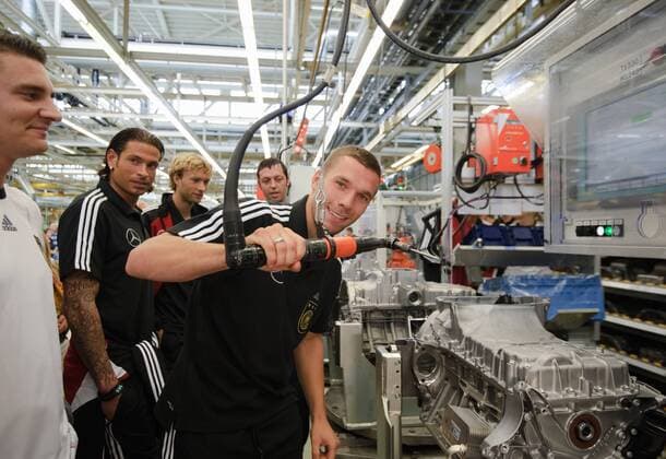 Lukas PODOLSKI (Deutschland) mit einem Werkzeug am Band der Fertigung, Hinter ihm v.l. : Torwart TIM WIESE und Simon ROLFES Werksführung der deutschen Fussball Nationalmannschaft im Motorenwerk von Mercedes-Benz in Bad Cannstatt Stuttgart am 9.8.2011. o00 Wirtschaft
