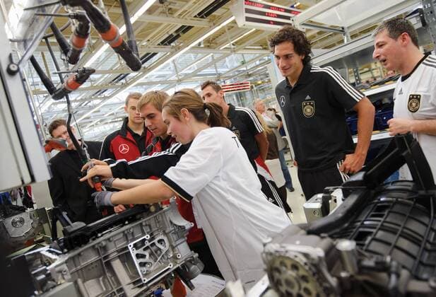 Eine Mitarbeiterin von Mercerdes-Benz zeigt den Spielern der Nationalmannschaft ihre Arbeit am Band. Kapitaen Spielfuehrer Mannschaftskapitaen Philipp LAHM (Deutschland) legt Hand an. Torwart Manuel NEUER (Deutschland, Miroslav KLOSE (Deutschland), Mats HUMMELS (DFB Deutschland), (von links), schauen zu. Fussball: Werksfuehrung der deutschen Fussball- Nationalmannschaft der Maenner am 09.08.2011 im Motorenwerk Bad Cannstatt, Stuttgart, 09.08.2011  o00 Wirtschaft Fan