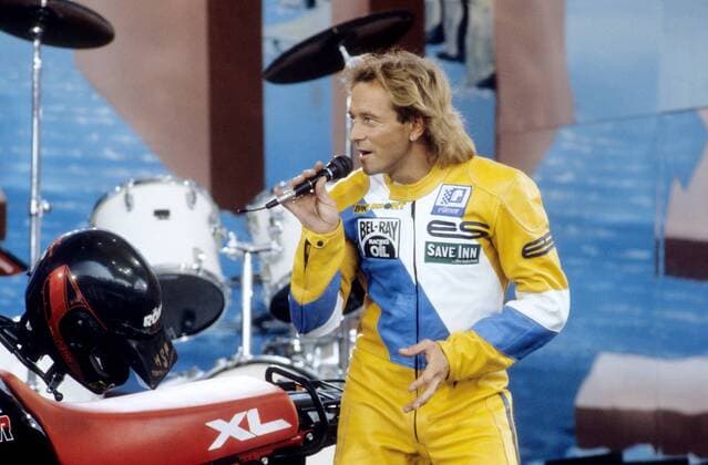 Egon Müller (Motorsportler) 09 87 ru Egon Müller während der IFA Internationale Funkausstellung in Berlin im September 1987 Deutschland deutsch Deutscher Mann Motorsport Motocross Rennsport Speedway Speedwayfahrer Fahrer Motorrad Motorradfahrer Motorradsport Sänger Musiker Amadeus Liszt german racing Overall sportlich Bühne Auftritt quer halb stehend singend Mikrofon haltend singen Berliner Messe Ausstellung Technik