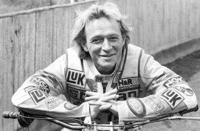 Egon Müller (Motorsportler) 08 88 dar Egon Müller am Rande von Dreharbeiten zu Die Männer vom K3 im August 1988 Deutschland deutsch Deutscher Motorsport Motocross Rennsport Speedway Speedwayfahrer Fahrer Motorrad Motorradfahrer Motorradsport Sänger Musiker Amadeus Liszt german racing Overall sportlich Motorrad Lenker quer halb aufgestützt aufstützend lächelnd sprechend gestikulierend draußen sw