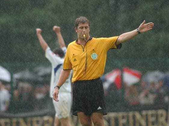 Robert Hoyzer (Schiedsrichter) 08 04 hör Mann Fußball Profifußball Bundesliga Pokal Pokalspiel DFB Schiedsrichter Unparteiischer kurzhaarig dunkelhaarig sportlich Trikot leger quer halb stehend draußen Spielfeld Partie Spiel Gestik gestikulierend Augen zu geschlossen pfeifend Pfeife Regen nass Nässe durchnässt Logo Pokalspiel SC Paderborn 07 gegen Hamburger SV (HSV) am 21.08.2004 in Paderborn (Ergebnis 4:2)