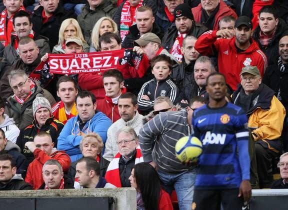 A Liverpool fan holds up a Luis Suarez scarf behind Manchester Uniteds Patrice Evra. Liverpool FC v Manchester United in the FA Cup Fourth Round sponsored by Budweiser at ANFIELD, Liverpool. 28th January 2012. EDITORIAL USE ONLY. No use with unauthorised audio, video, data, fixture lists, club league logos or live services. Online in-match use limited to 120 images, no video emulation. No use in betting, games or single club league player publications.