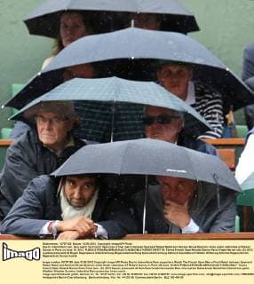 Due to intermittent rain, fans watch the French Open men s final match between Spaniard Rafael Nadal and Serbian Novak Djokovic while under umbrellas at Roland Garros in Paris on June 10, 2012.  PAR20120610718