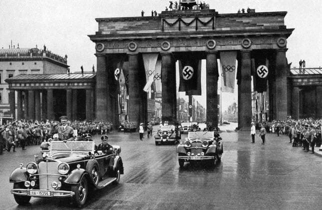 1936 Olympics, Berlin - Adolf Hitler in an open top car leading a fleet of cars through the Brandenburg Gate past spectators on its way to the 1936 Olympic Games. (Der Fuhrer Adolf Hitler, schirmherr der Olympischen Spiele, begibt such durch das Spalier der begeisterten Volksmenge zum Reichssportfeld, um die Spiele feierlich zu eroffnen) Â  UnitedArchives00834924
