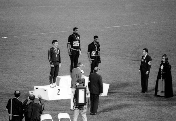 1968 Olympic Games, Mexico City America s gold and bronze medallists Tommie Smith (centre) and John Carlos (right) raise their arms as a Black Power gesture during the Olympic Awards Ceremony. Smith had set a world record of 19.8 seconds in the 200 metre race. Each man wore a black glove on one hand and raised it, with fist clenched as the US flag was raised. Perter Norman from Australia (left) won the silver medal. 16th October 1968.  UnitedArchives00835258