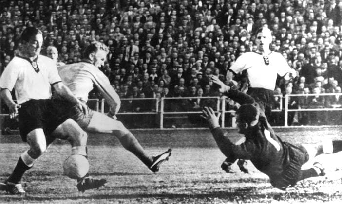 24th June 1958: World Cup semi-final. Germany versus Sweden: Photo shows: German centre-half, Herbert Erhardt (left) beats Swedish centre-forward Aone Simonsson to the ball during the match in Gothenburg. At right is Fritz Herkenrath, the German goalkeeper, who dives for the ball. German full-back, Georg Stollenwerk is shown in the right background.  UnitedArchives01009392