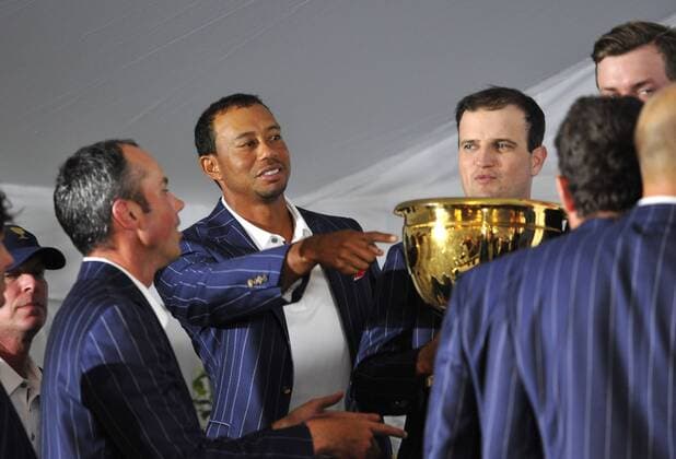 United States Team member Tiger Woods (C) directs teammate Zach Johnson (R) to pass the Presidents Cup down the line for the photo during a news conference following the 2013 Presidents Cup at Muirfield Village Golf Club in Dublin, Ohio on October 6, 2013. The United States defeated the International Team 18.5 to 15.5 to retain the Presidents Cup.  BKX2013100633