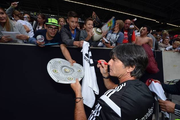 Deutschland Training --- Fussball --- International --- 01.09.2014 Joachim Jogi Löw, Loew (Trainer Deutschland), schreibt ein Autogramm auf die Meisterschale, im Hintergrund Fans, Anhänger, Anhaenger, Zuschauer, Groupies, Autogrammjäger, Autogrammjaeger, halbe Figur, Highlight