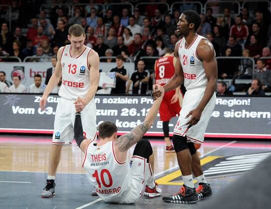 10.12.2014 - Basketball - Saison 2014 2015 - Eurocup : Brose Baskets Bamberg - SIG Straßburg - HMI - Janis Strelnieks (13, Brose Baskets Bamberg) und Trevor Mbakwe (21, Brose Baskets Bamberg) helfen Daniel Theis (10, Brose Baskets Bamberg) auf