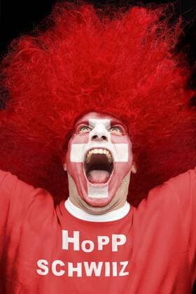 Schreiender junger Mann, Fußballfan, mit Gesichtsbemalung mit schweizerischer Nationalflagge und Shirt mit Aufschrift Hopp Schwiiz iblart02220628.jpg