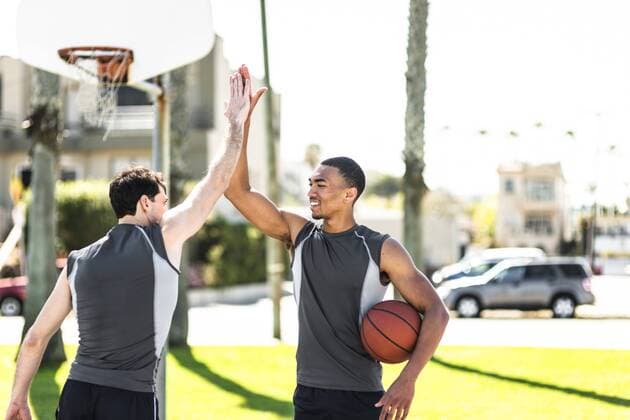Two young men high-fiving on outdoor basketball court model released Symbolfoto  LEF000113