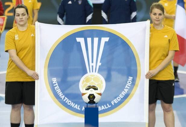 23. Handball-Weltmeisterschaft der Frauen 2017; Handball-WM, Viertelfinale in Leipzig; Frankreich - Montenegro (12.12.2017) Zwei Helferinnen der Handball-WM halten eine Fahne der International Handball Federation (IHF), davor ist ein Spielball Game Ball der Viertelfinals zu sehen. Leipzig Sachsen Deutschland