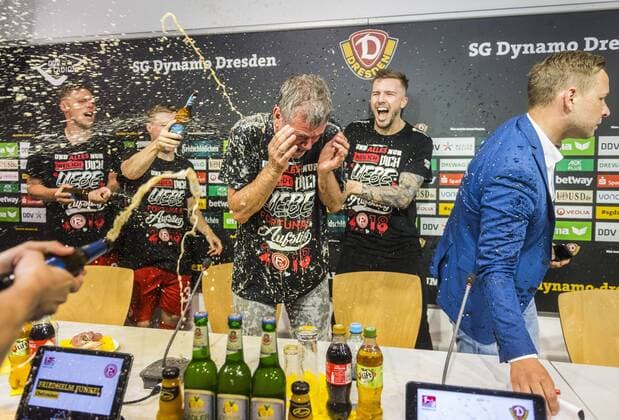Fußball, 2. Bundesliga, Saison 2017 2018, SG Dynamo Dresden, 32. Spieltag, SG Dynamo Dresden - Fortuna Düsseldorf (28.04.2018), DDV - Stadion, Dresden. Düsseldorfs Trainer Friedhelm Funkel wird von seinen Spielern nach dem Aufstieg in die Bundesliga während der Pressekonferenz mit Bier geduscht. Dynamos Pressesprecher Henry Buschmann (re.) verlässt das Podium. *** Football 2 Bundesliga Season 2017 2018 SG Dynamo Dresden 32 Matchday SG Dynamo Dresden Fortuna Dusseldorf 28 04 2018 DDV Stadion Dresden Dusseldorf coach Friedhelm Funkel is showered with beer by his players after the promotion to the Bundesliga during the press conference Dynamos press officer Henry Buschmann re leaves the podium RM001