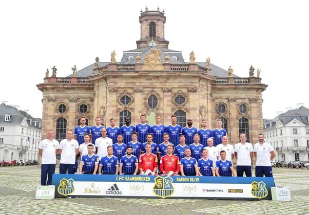 Das Team des 1. FC Saarbrücken am Donnerstag (12.07.2018) vor der Ludwigskirche in Saarbrücken. Im Bild: Obere Reihe (v.l.) Marco Holz ( 14), Macel Carl ( 22), Steven Zellner ( 5), Alexandre Mendy ( 4), Benjamin Kessel ( 15), Oliver Oschkenat ( 3), Nino Miotke ( 28), Jose Pierre Vunguidica ( 9), Sebastian Jacob ( 24) und Marco Kehl-Gomez. Mittlere Reihe: (v.l.) Robert Roelofsen (Co-Trainer), Dirk Lottner (Cheftrainer), Christoph Fuhr (Athletiktrainer), Heinz Böhmann (Torwart-Trainer), Gillian Jurcher ( 21), Lukas Quirin ( 31), Markus Obernosterer ( 10), Manuel Zeitz ( 8), Tobias Jänicke ( 25), Pierre Fassnacht ( 29), Helmut Schwan (Betreuer), Rüdiger Schmid (Zeugwart), Paulo da Palma (Physiotherapeut) und Frank Kackert (Torwart-Trainer). Untere Reihe: (v.l.) Fatih Köksal ( 27), Sascha Wenninger ( 19), Fanol Perdedaj ( 17), Ricco Cymer ( 20), Daniel Batz ( 1), Martin Dausch ( 7), Markus Mendler ( 11) und Mario Müller ( 23).