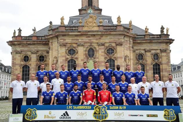 Das Team des 1. FC Saarbrücken am Donnerstag (12.07.2018) vor der Ludwigskirche in Saarbrücken. Im Bild: Obere Reihe (v.l.) Marco Holz ( 14), Macel Carl ( 22), Steven Zellner ( 5), Alexandre Mendy ( 4), Benjamin Kessel ( 15), Oliver Oschkenat ( 3), Nino Miotke ( 28), Jose Pierre Vunguidica ( 9), Sebastian Jacob ( 24) und Marco Kehl-Gomez. Mittlere Reihe: (v.l.) Robert Roelofsen (Co-Trainer), Dirk Lottner (Cheftrainer), Christoph Fuhr (Athletiktrainer), Heinz Böhmann (Torwart-Trainer), Gillian Jurcher ( 21), Lukas Quirin ( 31), Markus Obernosterer ( 10), Manuel Zeitz ( 8), Tobias Jänicke ( 25), Pierre Fassnacht ( 29), Helmut Schwan (Betreuer), Rüdiger Schmid (Zeugwart), Paulo da Palma (Physiotherapeut) und Frank Kackert (Torwart-Trainer). Untere Reihe: (v.l.) Fatih Köksal ( 27), Sascha Wenninger ( 19), Fanol Perdedaj ( 17), Ricco Cymer ( 20), Daniel Batz ( 1), Martin Dausch ( 7), Markus Mendler ( 11) und Mario Müller ( 23).
