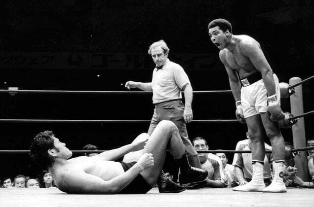 THE MUCH PUBLICIZED DOLLARS 10-MILLION CONTEST FOR THE MARTIAL ARTS CHAMPIONSHIP BTWEEN WORLD HEAVIWEIGHT BOXING CHAMPION MUHAMMAD ALI AND JAPAN S PRO WRESTLING CHAMPION ANTONIO INOKI AT THE NIPPON BUDOKAN HALL IN TOKIO ON JUNE 26 TUREND OUT THE WORST BOUT OF THE CENTURY. SEREVAL OF THE ESTIMATED 13,000 FANS SHOWED THEIR ANGER AND FRUSTRATION AS THE 15 ROUNDS BOUT ENDED IN A DRAW. DURING THE HOUR LONG BOUT,INOKI WAS LYING ON HIS BACK ON THE MAT WHILE ALI WAS CONSTANTLY CIRCLING,DANCING AWAY AND MAKING FACES AT THE JAPANESE WRESTLER.THERE WERE ONLY THREE TIMSE WHEN THE TWO ACTUALLY GRAPPLED WITH EACH OTHER. ALI MANAGED TO LAND A FEW JABS THROUGHOUT THE FIGHT,WHILE INOKI CONCENTRATED ON MAKING FLYING KICKS ON ALI S FOOT. PHOTO SHOWS ALI MAKING FACES AT THE JAPANESE WRESTLER IN THE 12 ROUNDS OF THEIR BOUT. .HPT WST BELGA  x85193318stx