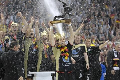 Vorschau Handball WM 2019 vom 10-27.01.2019 in Deutschland und Daenemark. Archivfoto; Siegerehrung, Markus BAUR (Mitte), hebt den Siegerpokal WM-Pokal in die Hoehe, bejubelt und beobachtet von den deutschen Nationalspielern, die goldene Kronen und kuenstliche Schnauzbaerte tragen, es wird mit Sekt gespritzt, Finale Finalspiel Endspiel Deutschland (GER)-Polen (POL) 29:24, am 04.02.2007 in Koeln, Weltmeister Deutschland Handball Weltmeisterschaft 2007 in Deutschland, vom 19.01. - 04.02.2007