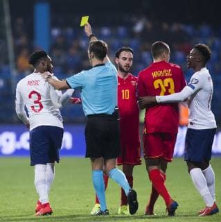 25th March 2019, Podgorica City Stadium, Podgorica, Montenegro; UEFA European Championships Qualification football, Montenegro versus England; Referee Aleksei Kulbakov of Belarus gives a yellow card to Danny Rose of England  ActionPlus12117788 NikolaxKrstic