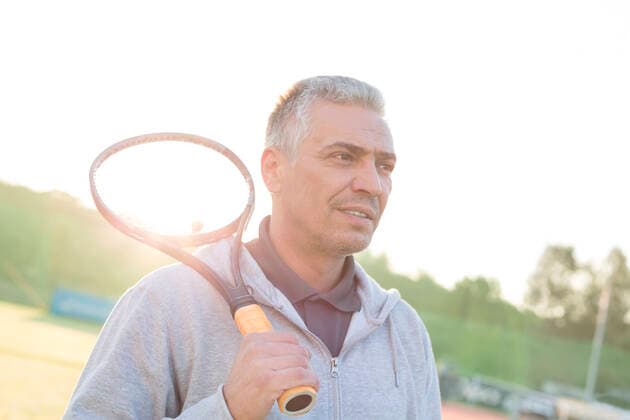 Back lit of confident mature man standing with tennis racket on court against clear sky INH_19064_13181