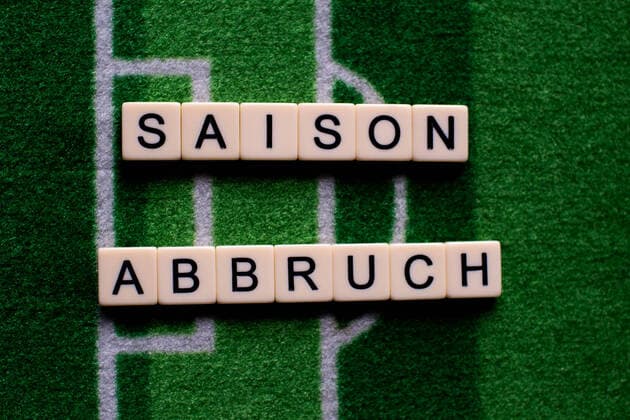 Das Coronavirus (Covid-19) verursacht Veranstaltungsabsagen von beispielsweise Fußballspielen der Bundesligaprofiligen auf unbestimmte Zeit und viele Auswirkungen, im Bild: Das Wort Saisonabbruch auf einem Fußballteppich. Deutschland
