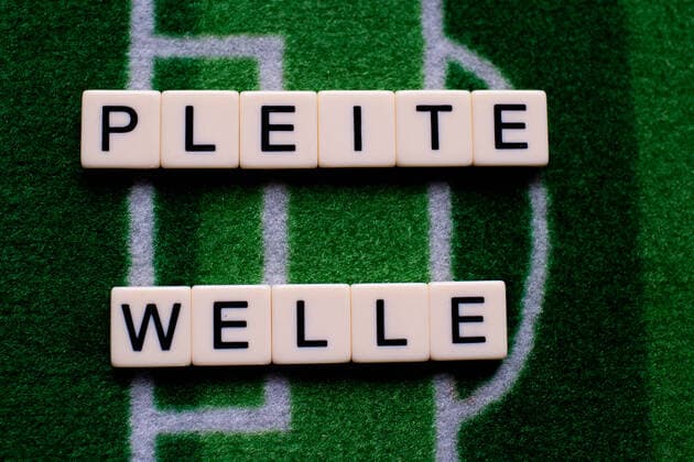 Das Coronavirus (Covid-19) verursacht Veranstaltungsabsagen von beispielsweise Fußballspielen der Bundesligaprofiligen auf unbestimmte Zeit und viele Auswirkungen, im Bild: Das Wort Pleitewelle auf einem Fußballteppich. Deutschland