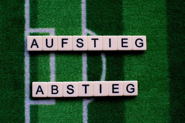 Das Coronavirus (Covid-19) verursacht Veranstaltungsabsagen von beispielsweise Fußballspielen der Bundesligaprofiligen auf unbestimmte Zeit und viele Auswirkungen, im Bild: Das Wort Aufstieg und Abstieg auf einem Fußballteppich. Deutschland