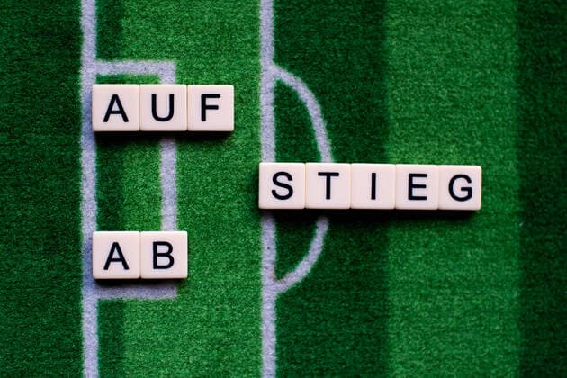 Das Coronavirus (Covid-19) verursacht Veranstaltungsabsagen von beispielsweise Fußballspielen der Bundesligaprofiligen auf unbestimmte Zeit und viele Auswirkungen, im Bild: Das Wort Aufstieg und Abstieg auf einem Fußballteppich. Deutschland
