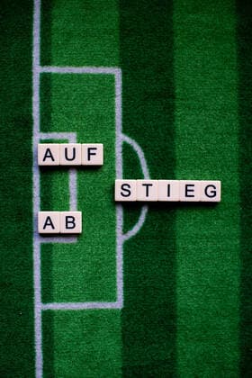 Das Coronavirus (Covid-19) verursacht Veranstaltungsabsagen von beispielsweise Fußballspielen der Bundesligaprofiligen auf unbestimmte Zeit und viele Auswirkungen, im Bild: Das Wort Aufstieg und Abstieg auf einem Fußballteppich. Deutschland