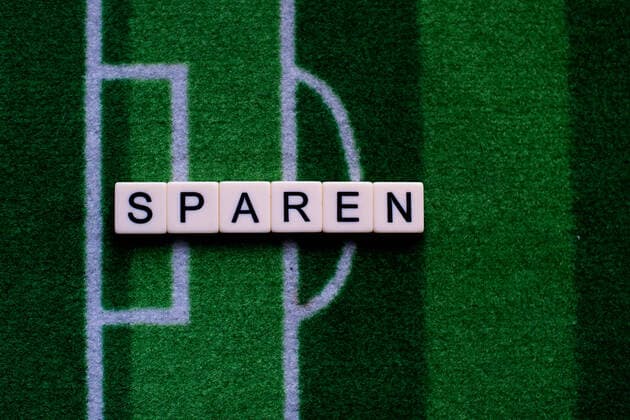 Das Coronavirus (Covid-19) verursacht Veranstaltungsabsagen von beispielsweise Fußballspielen der Bundesligaprofiligen auf unbestimmte Zeit und viele Auswirkungen, im Bild: Das Wort Sparen auf einem Fußballteppich. Deutschland