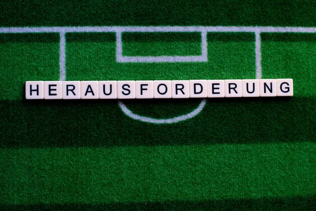 Das Coronavirus (Covid-19) verursacht Veranstaltungsabsagen von beispielsweise Fußballspielen der Bundesligaprofiligen auf unbestimmte Zeit und viele Auswirkungen, im Bild: Das Wort Herausforderung auf einem Fußballteppich. Deutschland