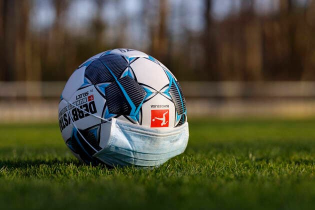 Der offizielle Spielball der Bundesliga Derbystar liegt mit Mundschutz auf einem Fußballplatz. Köln, 11.04.2020
