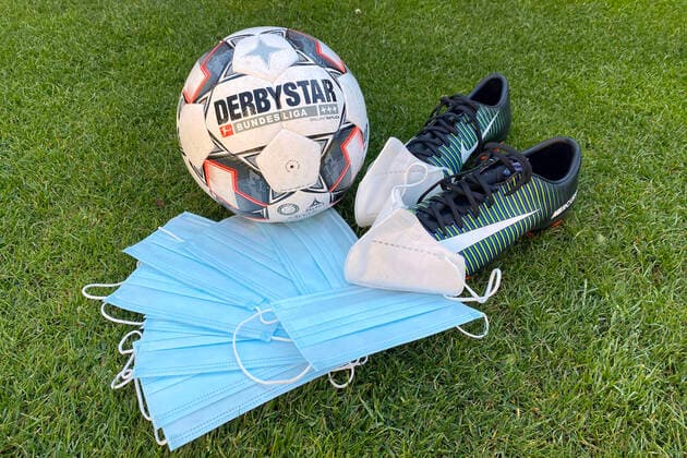 Themenfoto: Coronavirus Pandemie -Auswirkungen auf den Fussball. Mundschutzmasken,Masken liegen vor einem DERBYSTAR Spielball, Ball und ein paar Fussballschuhen. Feature,Randmotiv,allgemein.