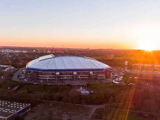 Fußball: FC Schalke 04: Bundesliga. Blick auf das Trainingsgelände des FC Schalke 04 mit der Veltins Arena und den Trainingsplätzen. Die Sonne geht am Horizont in Gelsenkirchen im Ruhrgebiet unter. In der Ferne sind Kühltürme der Raffinerien zu erkennen. *** Football FC Schalke 04 Bundesliga View of the training ground of FC Schalke 04 with the Veltins Arena and the training fields The sun is setting on the horizon in Gelsenkirchen in the Ruhr area Cooling towers of the refineries can be seen in the distance Copyright: xChristopherxNeundorf Kirchner-Mediax