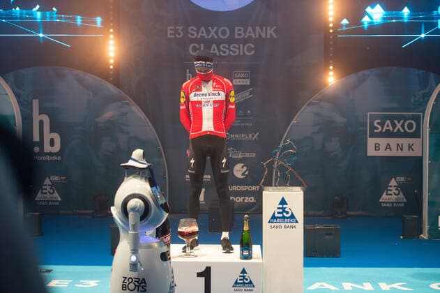 Radsport, E3 Harelbeke - Roboter führt Siegerehrung durch Kasper Asgreen (DEN DK - Deceuninck-Quick Step) gewinnt die 64. Austragung des E3-Preises und kann sich auf dem Podium feiern lassen - hier abgeschottet in der Sporthalle von Harelbeke ohne Zuschauer wegen der Covid-19 Corona Pandemie - Siegerehrung - Ehrung - Auszeichnung - Zeremonie - Zelebrierung - Ceremony - Jubel - Freude - Luck - Emotion - Emotionen - Mimik - Mimic - Gestik - Gestic - Querformat quer horizontal Event Veranstaltung: 64. E3 Saxo Bank Classic - Harelbeke nach to Harelbeke 203.9 km - Ort Location: Harelbeke - Region: West-Vlaanderen (Flandern) - Land Country: Belgien Belgium - Datum Date: 26.03.2021